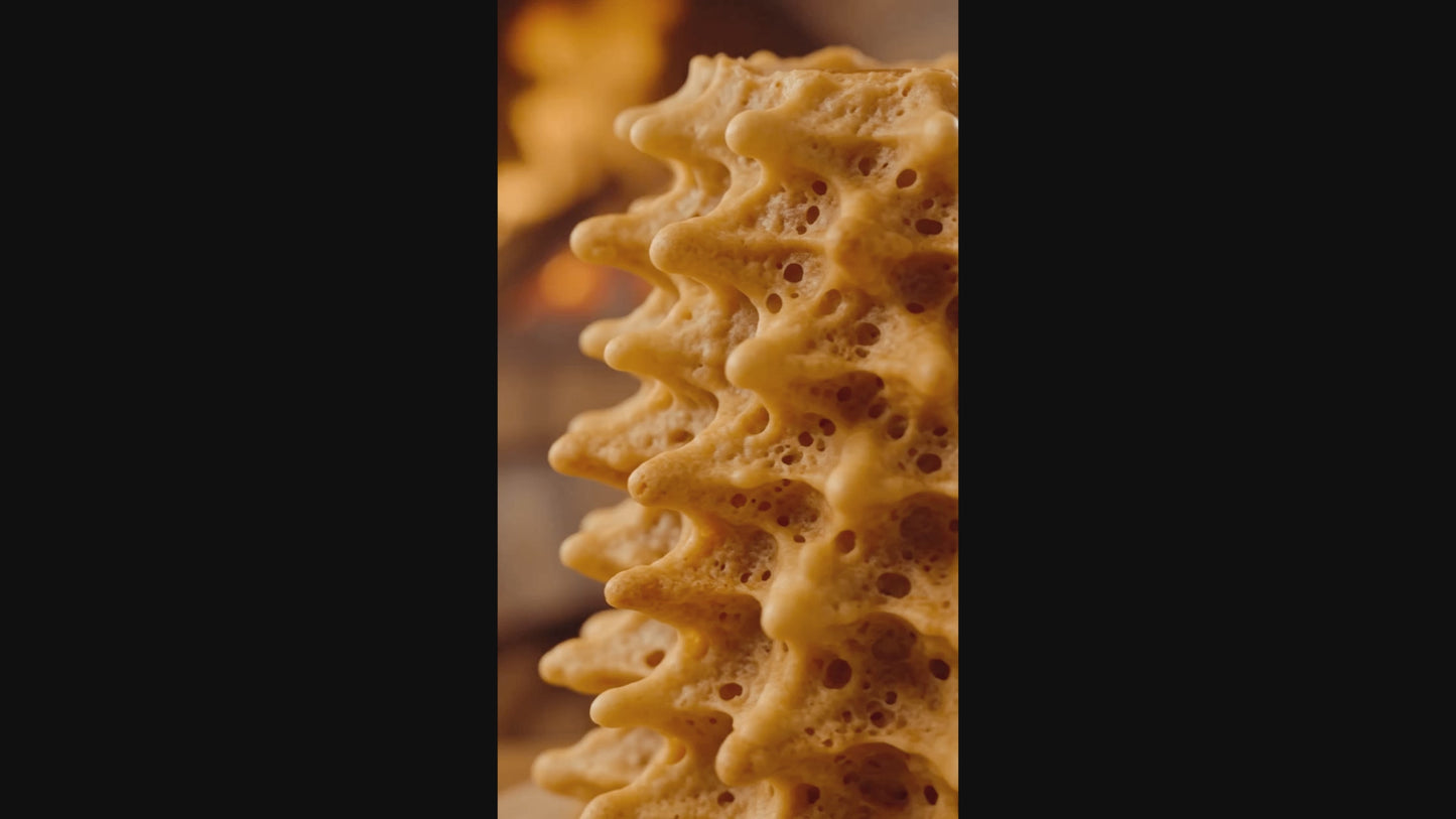 Cinematic Produktpräsentation eines echten litauischen Baumkuchens (Šakotis). Die Kamera zeigt in einer edlen Nahaufnahme die markanten, goldbraun gebackenen Spitzen des traditionellen Spießkuchens vor einem warmen, dunklen Hintergrund.